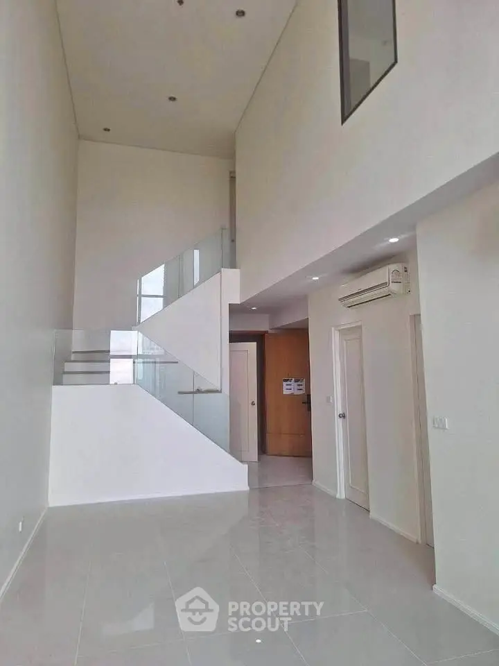 Spacious modern living room with high ceilings and sleek staircase in minimalist design.