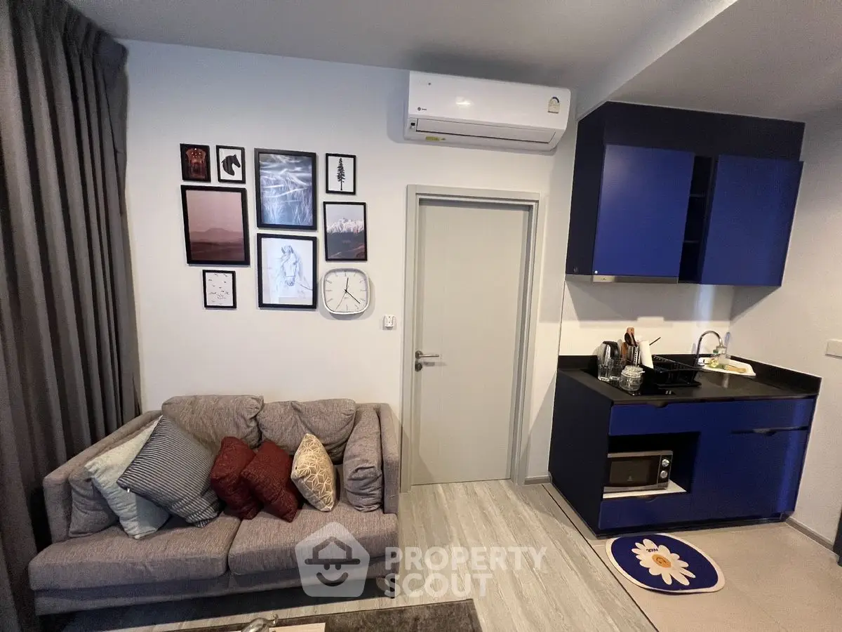 Modern studio apartment with cozy living area and compact kitchen featuring blue cabinets and wall art.