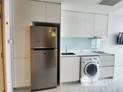 Modern kitchen with stainless steel appliances, including a large fridge and washing machine, complemented by white cabinetry and sleek countertops.