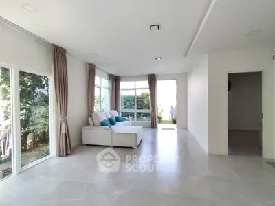 Spacious living room with large windows and garden view, featuring elegant tile flooring and cozy seating area.