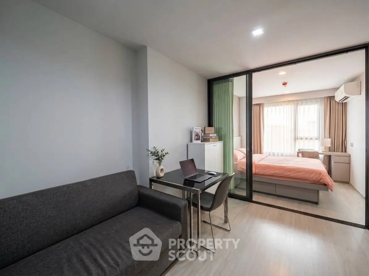 Modern studio apartment with open layout, featuring a cozy living area and a stylish bedroom separated by glass doors.
