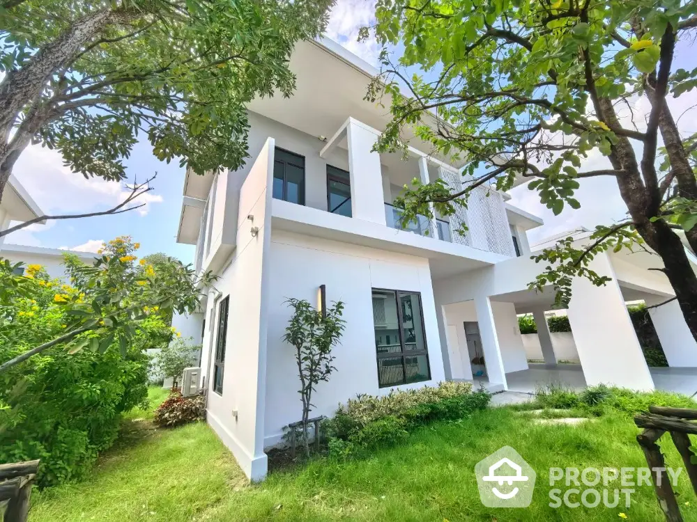 Modern white two-story house with lush green garden and trees