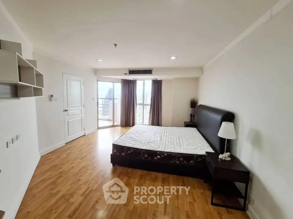 Spacious bedroom with wooden flooring and large window offering city views.
