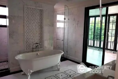 Luxurious bathroom with elegant freestanding bathtub and glass shower, overlooking a serene balcony view.