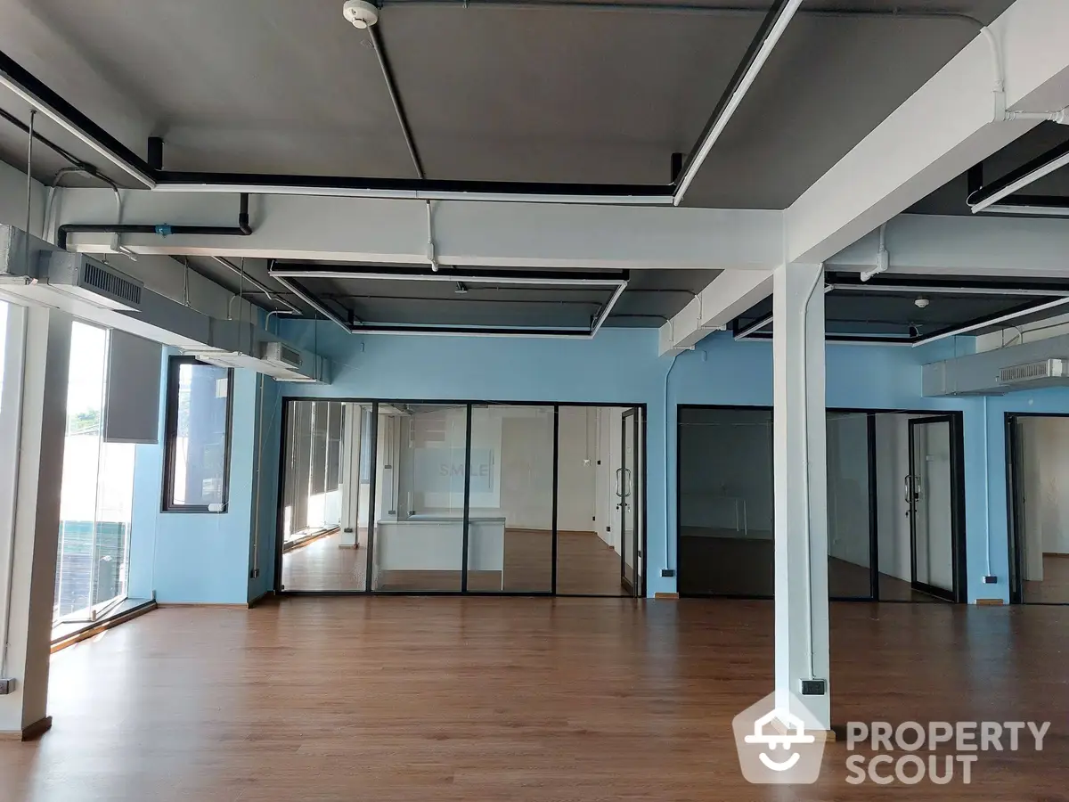 Expansive commercial space with wooden flooring, large windows, and modern ductwork, ideal for a bespoke office or studio.