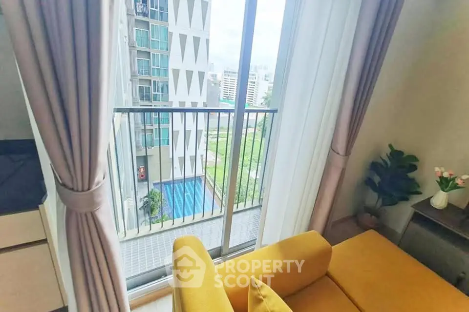 Modern living room with balcony view overlooking pool and cityscape, featuring stylish yellow sofa.