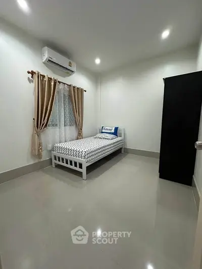 Minimalist bedroom with single bed, air conditioning, and sleek wardrobe in modern apartment.