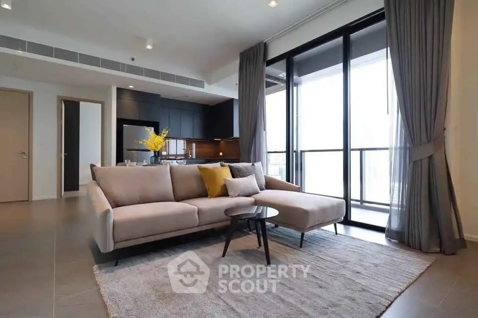 Modern living room with elegant sofa, floor-to-ceiling windows, and open kitchen layout.