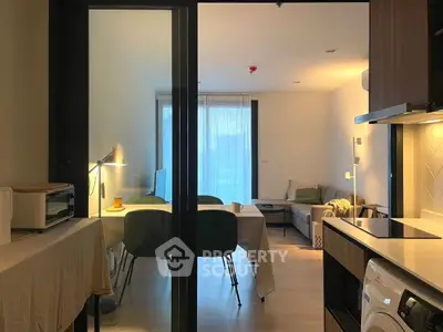 Modern open-plan living room with dining area and kitchen, featuring sleek furniture and natural lighting.