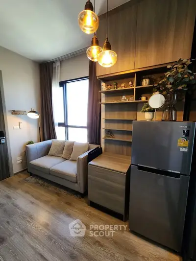 Modern living room with stylish lighting, cozy sofa, and sleek fridge in a compact apartment setting.