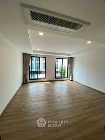 Spacious empty living room with large windows and wooden flooring in modern apartment.