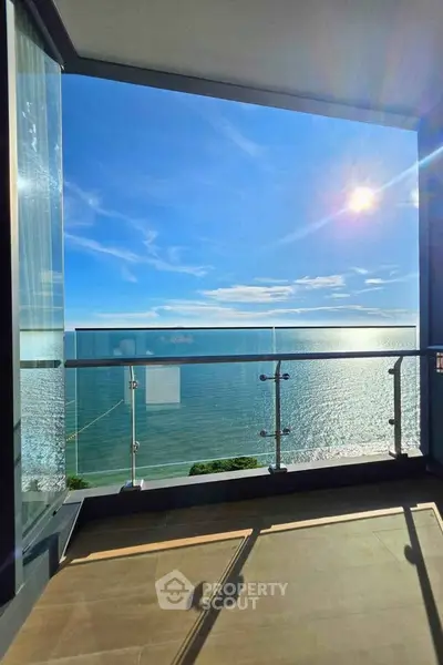 Stunning ocean view from a modern balcony with glass railing and sunny skies.
