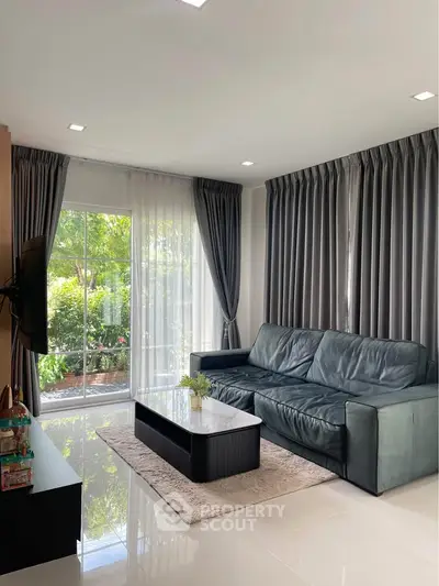Elegant living room with large windows and garden view, featuring a stylish sofa and modern decor.