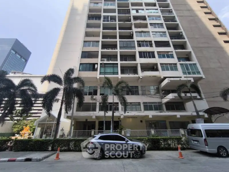 Modern high-rise building exterior with palm trees and parked cars in urban setting.