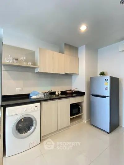 Modern kitchen with sleek cabinets, washing machine, and stainless steel fridge in a compact layout.