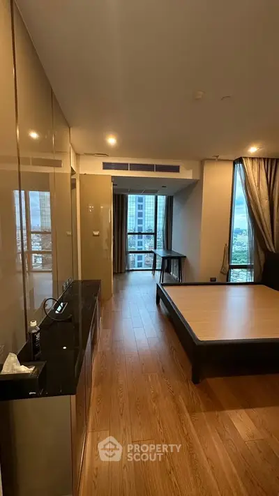 Spacious bedroom with wooden flooring and large windows offering city views