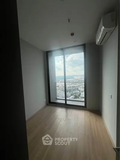 Spacious room with large window offering stunning cityscape view, featuring sleek wooden flooring and modern air conditioning.