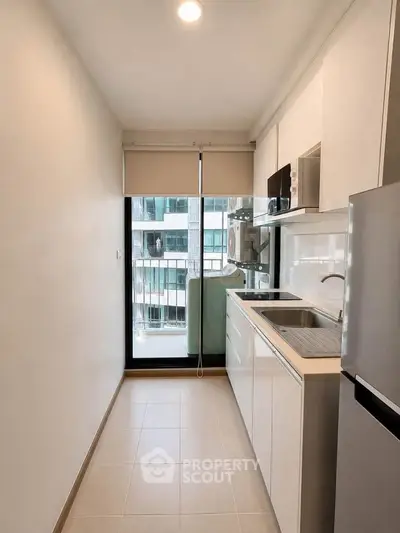 Modern compact kitchen with sleek white cabinetry and large window view in urban apartment.