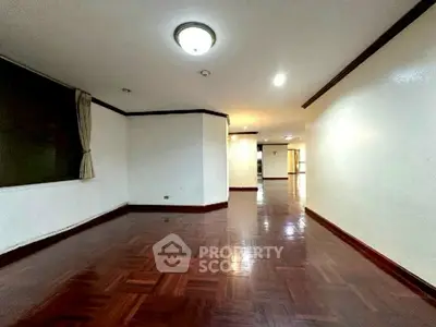 Spacious empty living room with polished wooden floors and bright lighting.