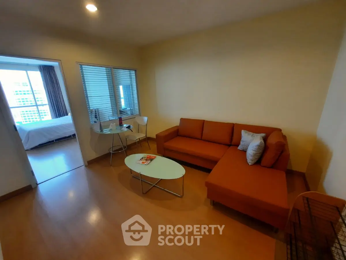 Modern living room with orange sofa and view into bedroom, featuring sleek wooden flooring.
