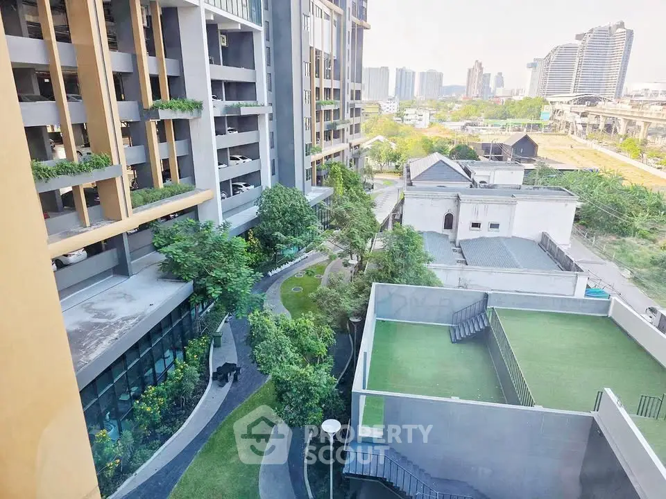 Modern urban apartment complex with lush green landscaping and city skyline view.