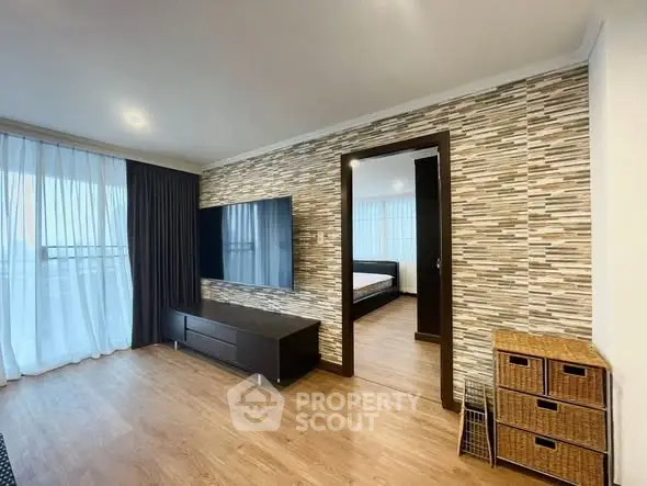 Modern living room with stylish decor and large TV, featuring a glimpse into a cozy bedroom.