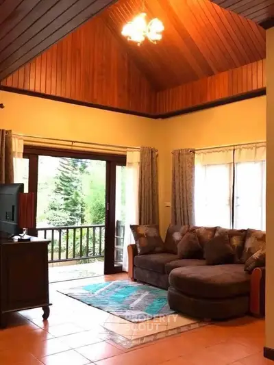 Charming living room with high wooden ceiling and cozy seating area overlooking lush greenery.