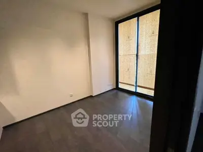 Spacious empty room with dark flooring and large window, ideal for customization.