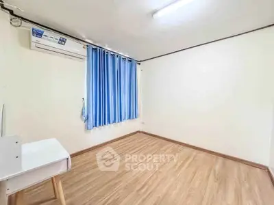 Spacious empty room with wooden flooring and blue curtains, ideal for customization.