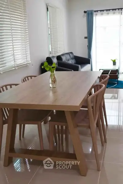 Modern dining area with wooden table and chairs, adjacent to cozy living room with natural light.
