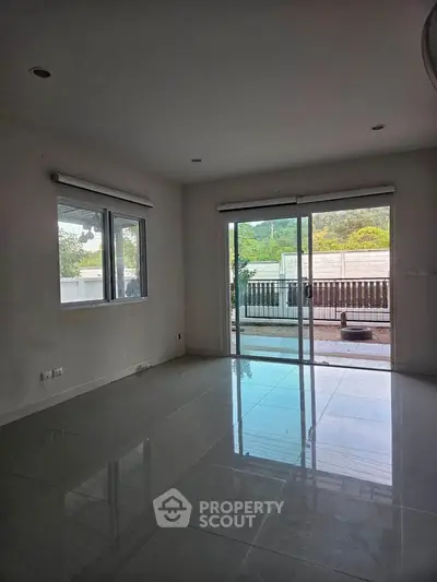 Spacious living room with large windows and sliding doors leading to a patio, offering natural light and outdoor access.