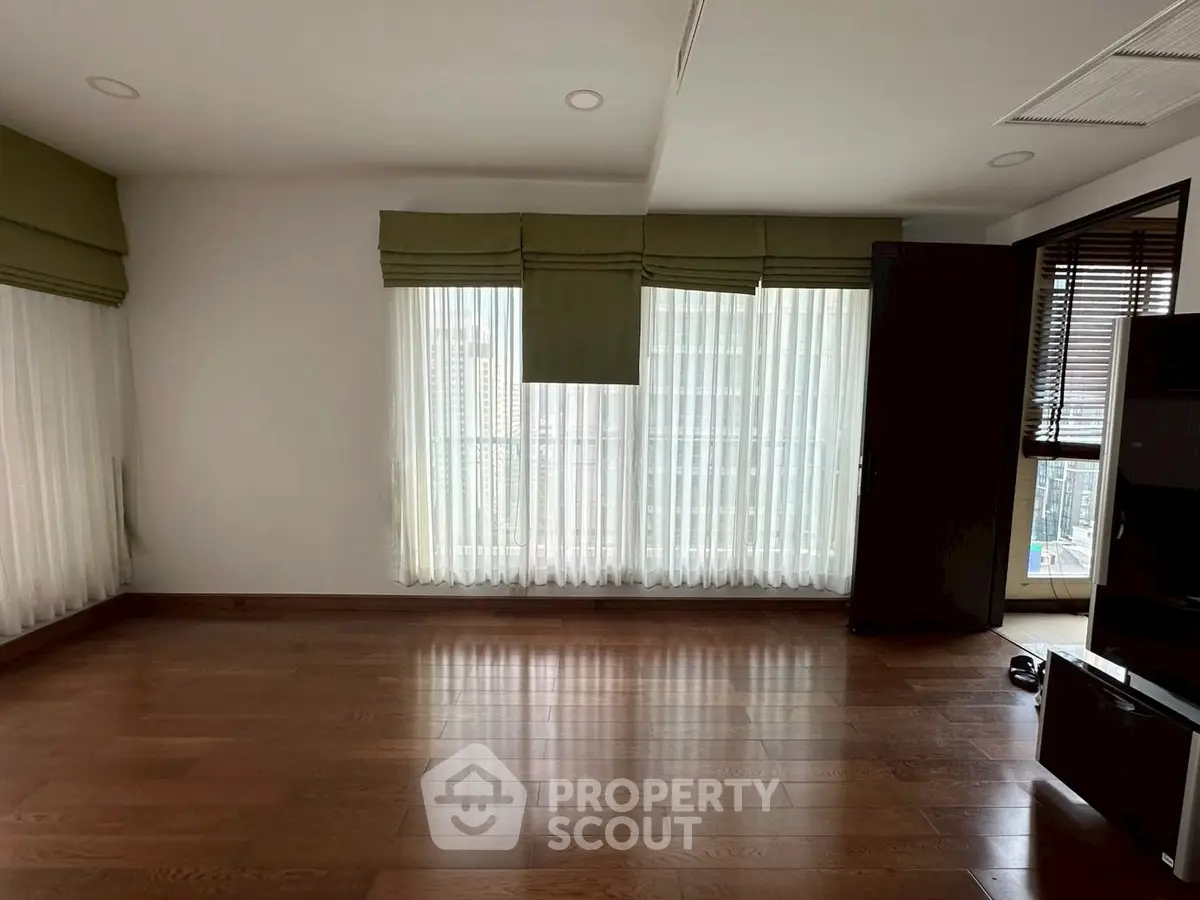 Spacious living room with wooden flooring and large windows for natural light.
