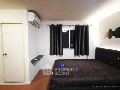 Modern bedroom with sleek black bed and air conditioning unit, featuring elegant dark curtains.