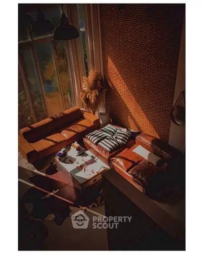 Luxurious living room with leather sofas and brick accent wall, bathed in natural light.