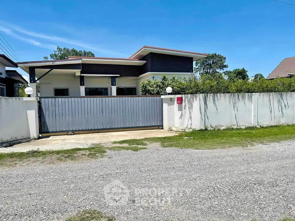 Modern single-story house with gated entrance and lush greenery