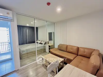 Modern living room with brown leather sofa and glass partition leading to bedroom in stylish apartment.