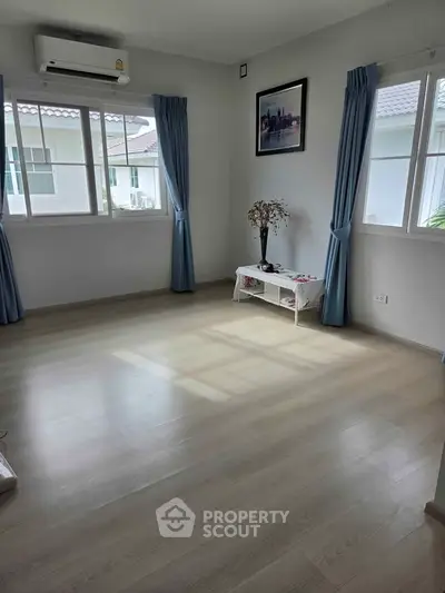 Bright and airy room with large windows and wooden flooring, perfect for a cozy living space.