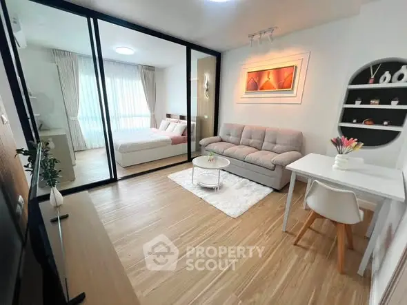 Modern open-plan living room with cozy sofa and stylish decor adjacent to a bedroom with glass partition.