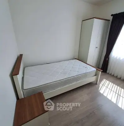 Minimalist bedroom with single bed and wardrobe, featuring natural light and wooden accents.