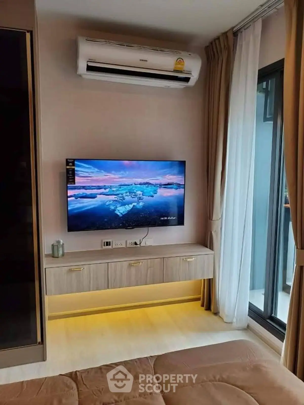 Modern living room with wall-mounted TV and air conditioning, featuring a cozy ambiance and natural light.
