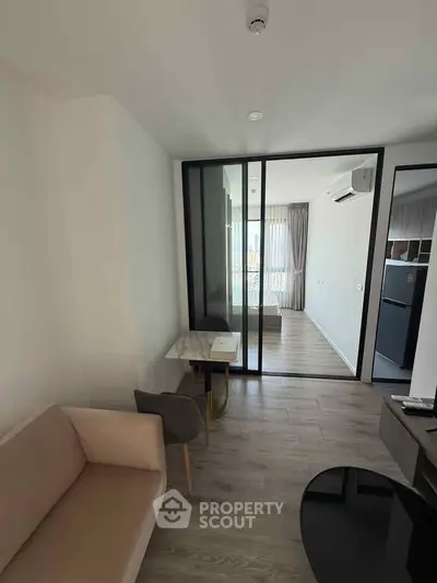 Modern apartment interior with glass partition, cozy seating, and sleek flooring.