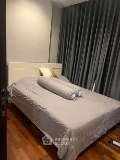 Cozy bedroom with elegant gray curtains and wooden flooring, featuring a comfortable bed with plush pillows.