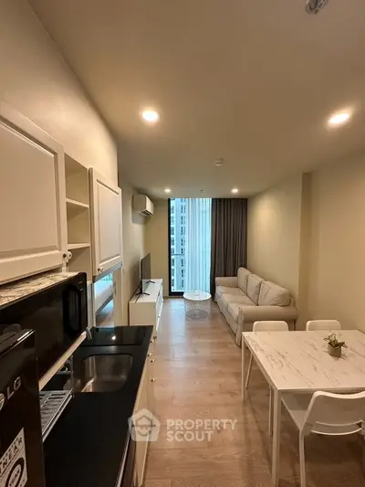 Modern living room with open kitchen, featuring sleek furniture and natural light.