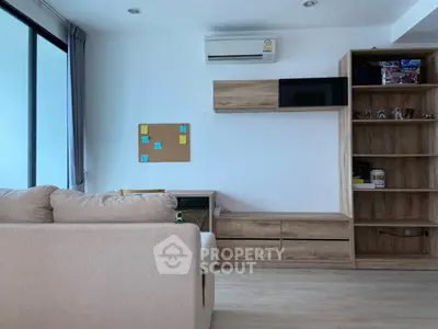 Modern living room with beige sofa, wall-mounted TV, and wooden shelving unit.