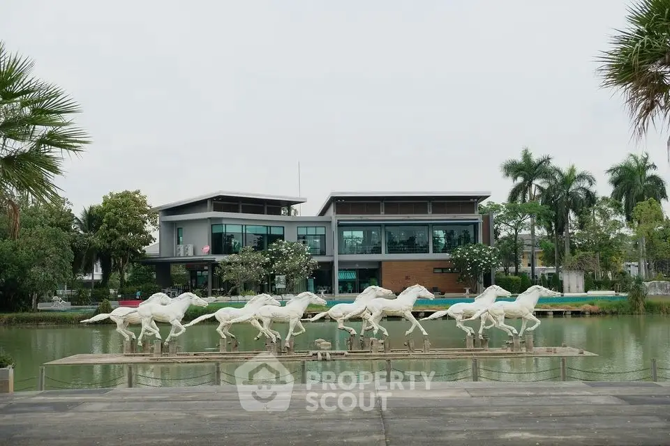 Luxurious modern building with horse sculptures by a serene pond, surrounded by lush greenery.