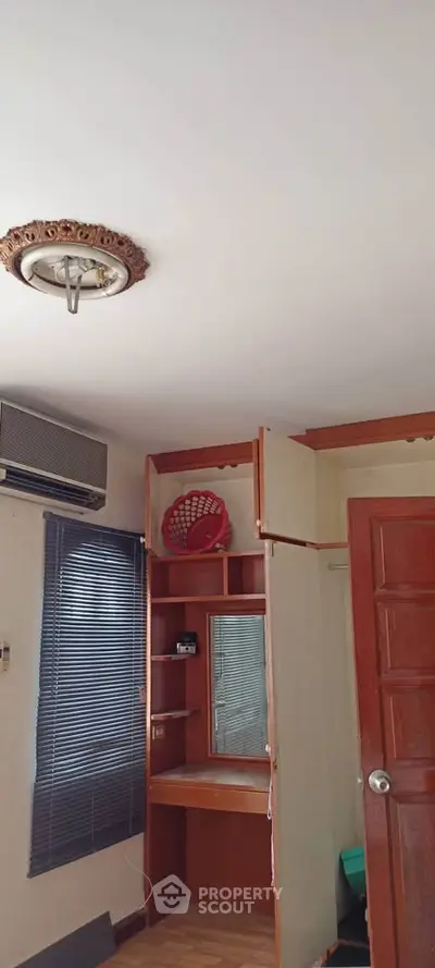 Cozy bedroom with built-in wooden wardrobe and air conditioning unit, perfect for comfortable living.