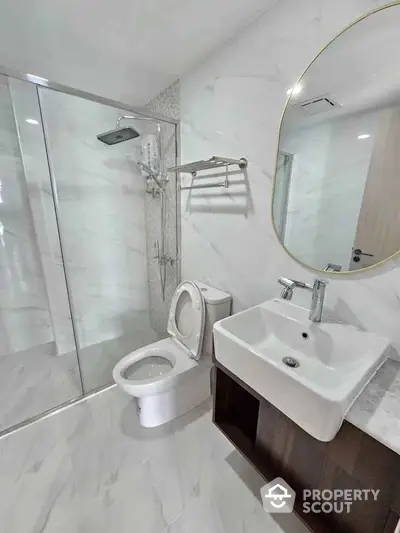 Modern bathroom with glass shower, round mirror, and sleek fixtures.