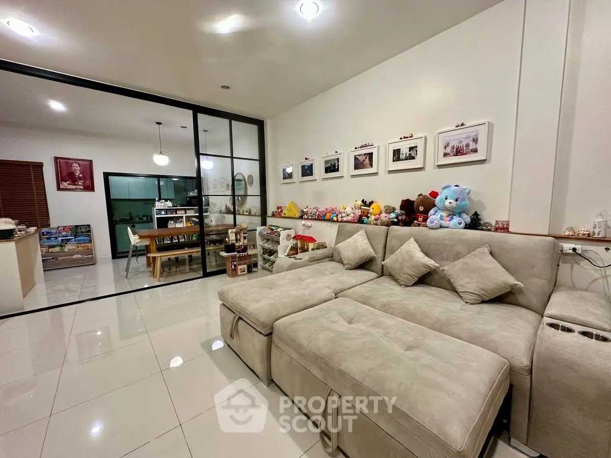 Spacious living room with plush sofa and glass partition leading to dining area.