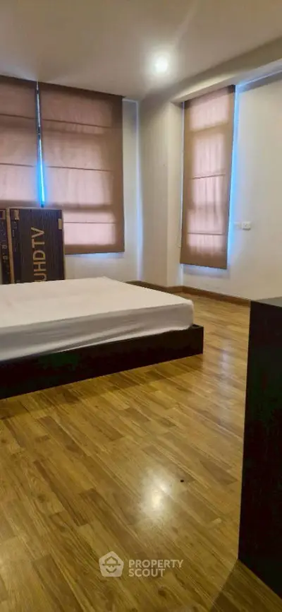 Spacious bedroom with wooden flooring and large windows for natural light.