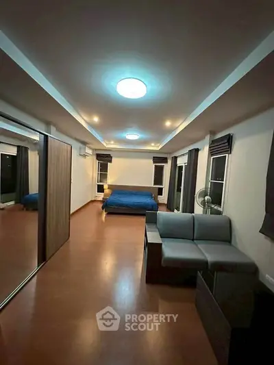 Spacious bedroom with modern lighting and wooden flooring, featuring a cozy bed and a stylish sofa.